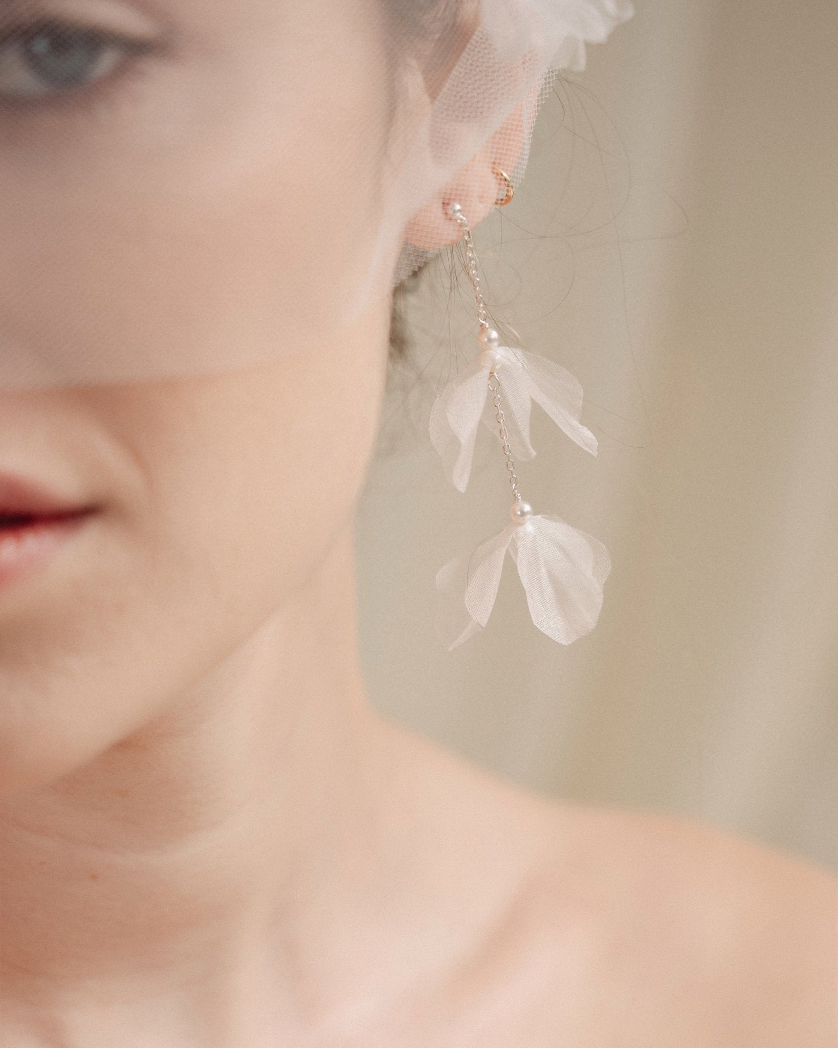 Bride wears an ivory tulle veil with face-framing silk flowers with coordinating silk flower and pearl long drop earrings