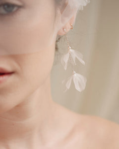 Bride wears an ivory tulle veil with face-framing silk flowers with coordinating silk flower and pearl long drop earrings