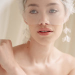 Bride wears an ivory tulle veil with face-framing silk flowers with coordinating silk flower and pearl long drop earrings