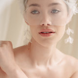 Bride wears an ivory tulle veil with face-framing silk flowers with coordinating silk flower and pearl long drop earrings