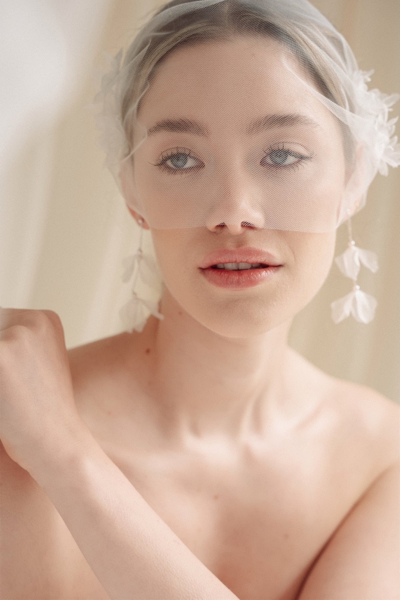 Bride wears an ivory tulle veil with face-framing silk flowers with coordinating silk flower and pearl long drop earrings