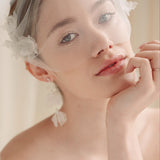 Bride wears an ivory tulle veil with face-framing silk flowers with coordinating silk flower and pearl long drop earrings