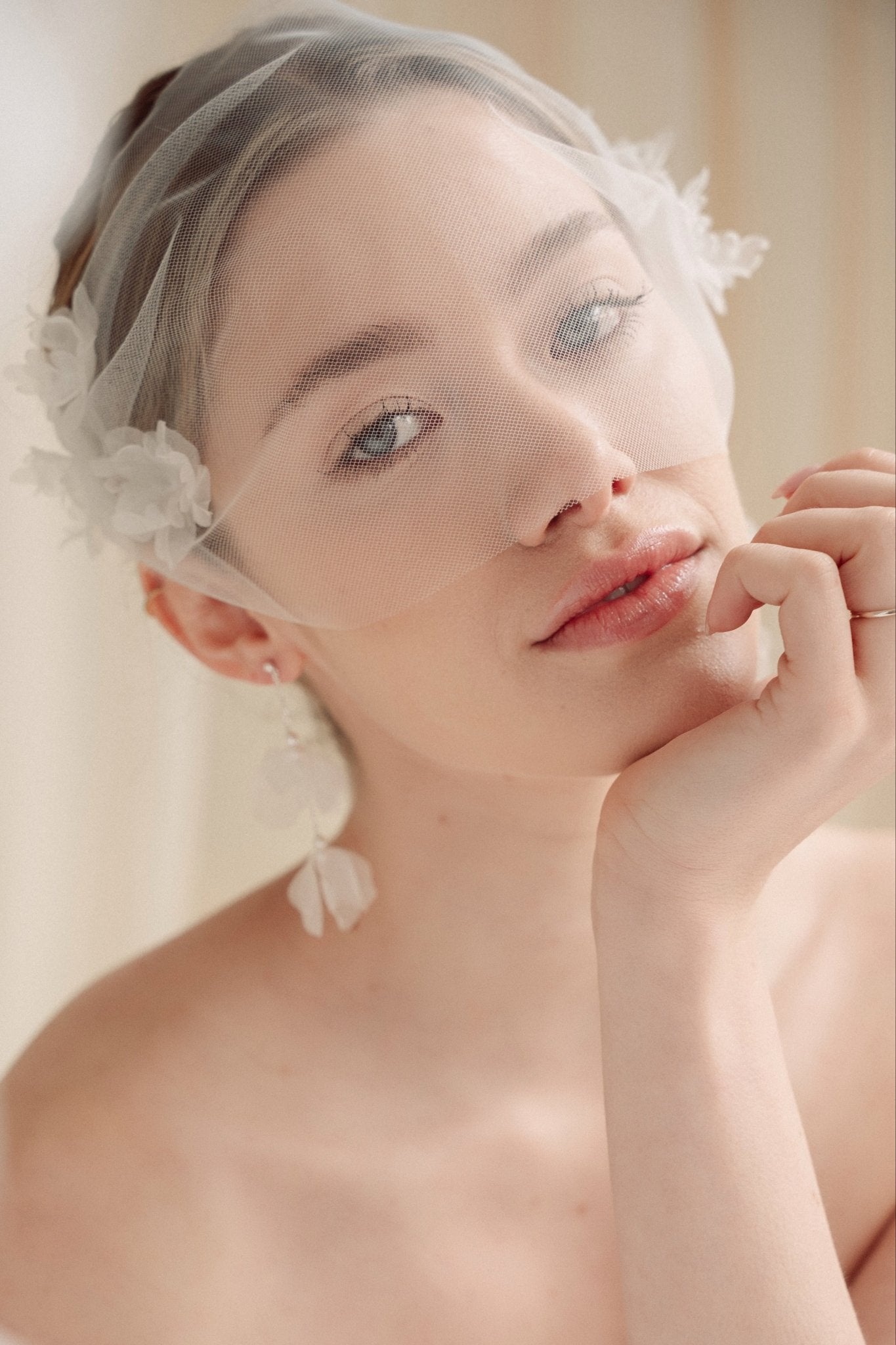 Bride wears an ivory tulle veil with face-framing silk flowers with coordinating silk flower and pearl long drop earrings