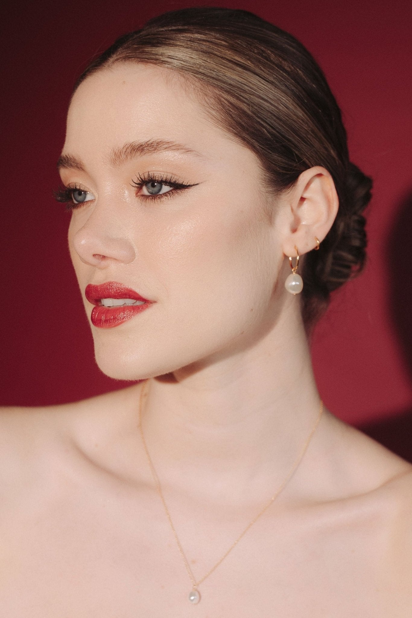 Bride wearing gold hoop earrings with a single vegan baroque pearl with a sleek low bun hair style and a matching gold pearl necklace