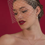 bride wears a crystal birdcage veil with gold hoop pearl earrings and matching necklace