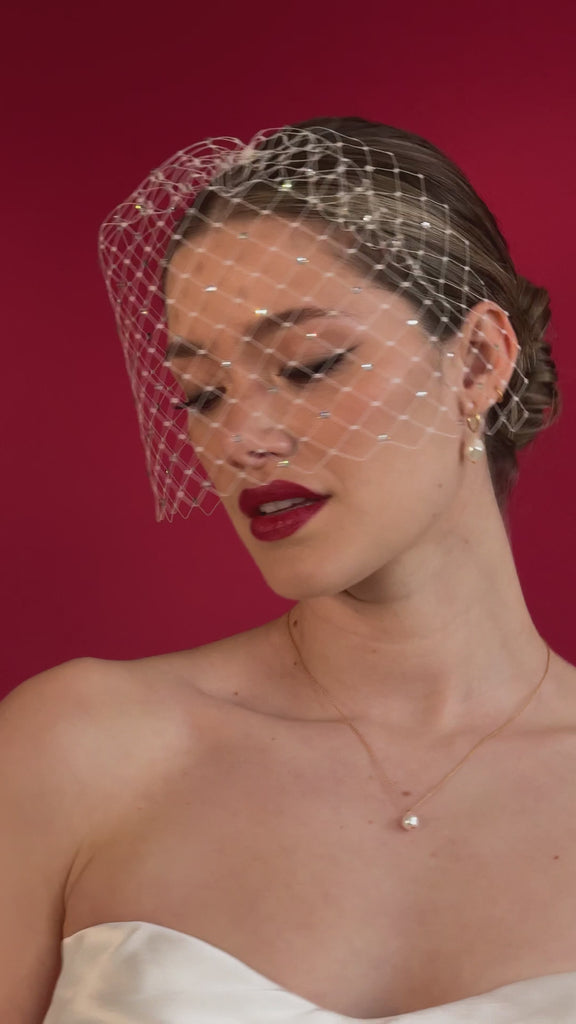 bride wears a crystal birdcage veil with gold hoop pearl earrings and matching necklace