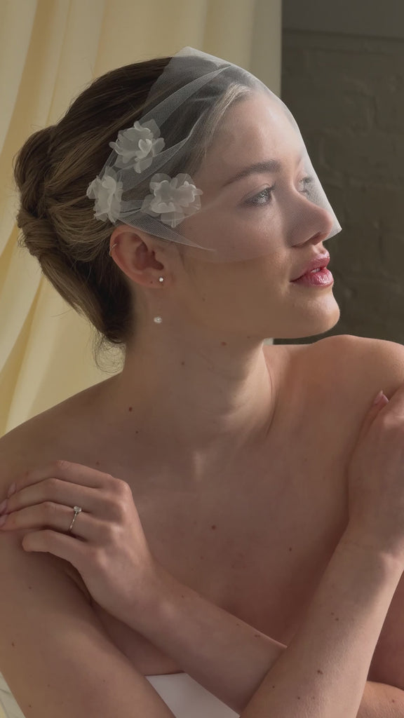 bride wears dainty pearl drop earrings with a tulle mask veil and frace-framing silk flowers