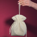Hand holding a small ivory lace and satin drawstring bag against a red background