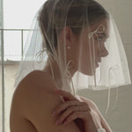 bride wears a micro drop veil down to her shoulders with long bow details and a crystal and pearl set of stud drop earrings