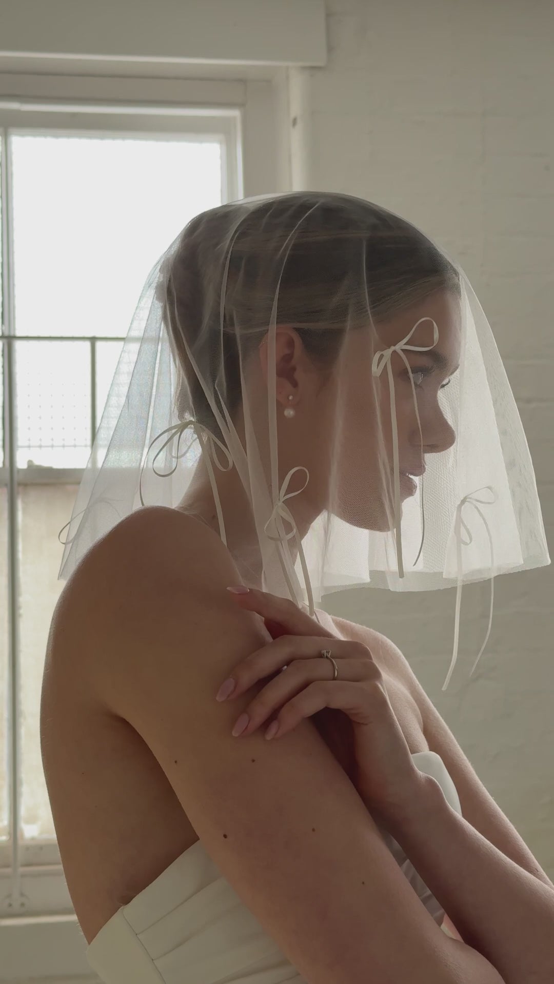 bride wears a micro drop veil down to her shoulders with long bow details and a crystal and pearl set of stud drop earrings