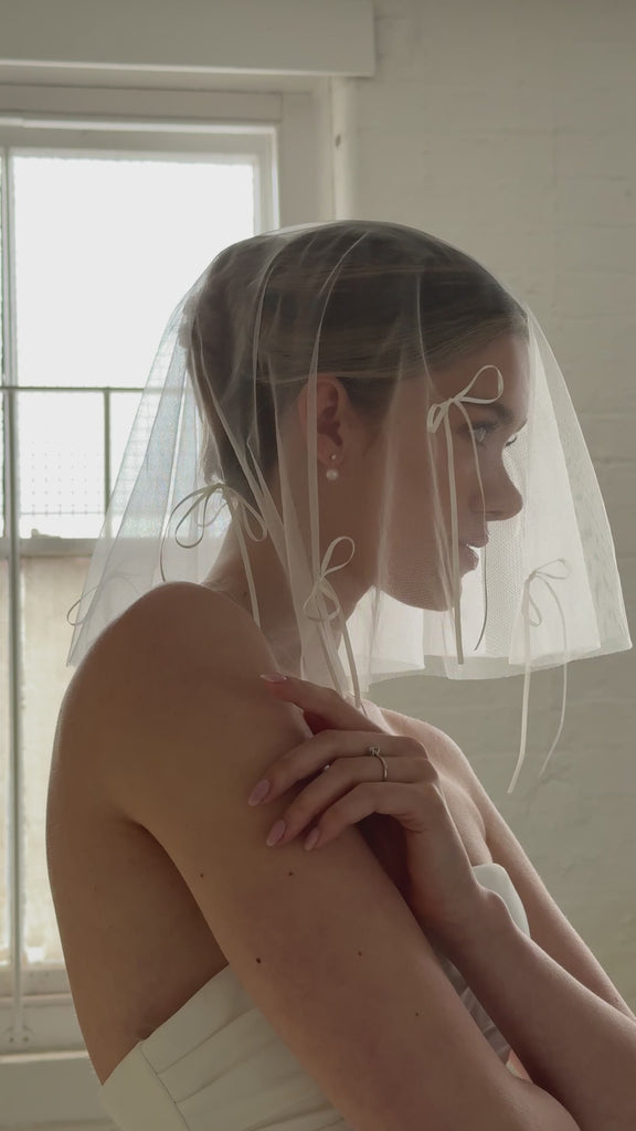 bride wears a micro drop veil down to her shoulders with long bow details and a crystal and pearl set of stud drop earrings