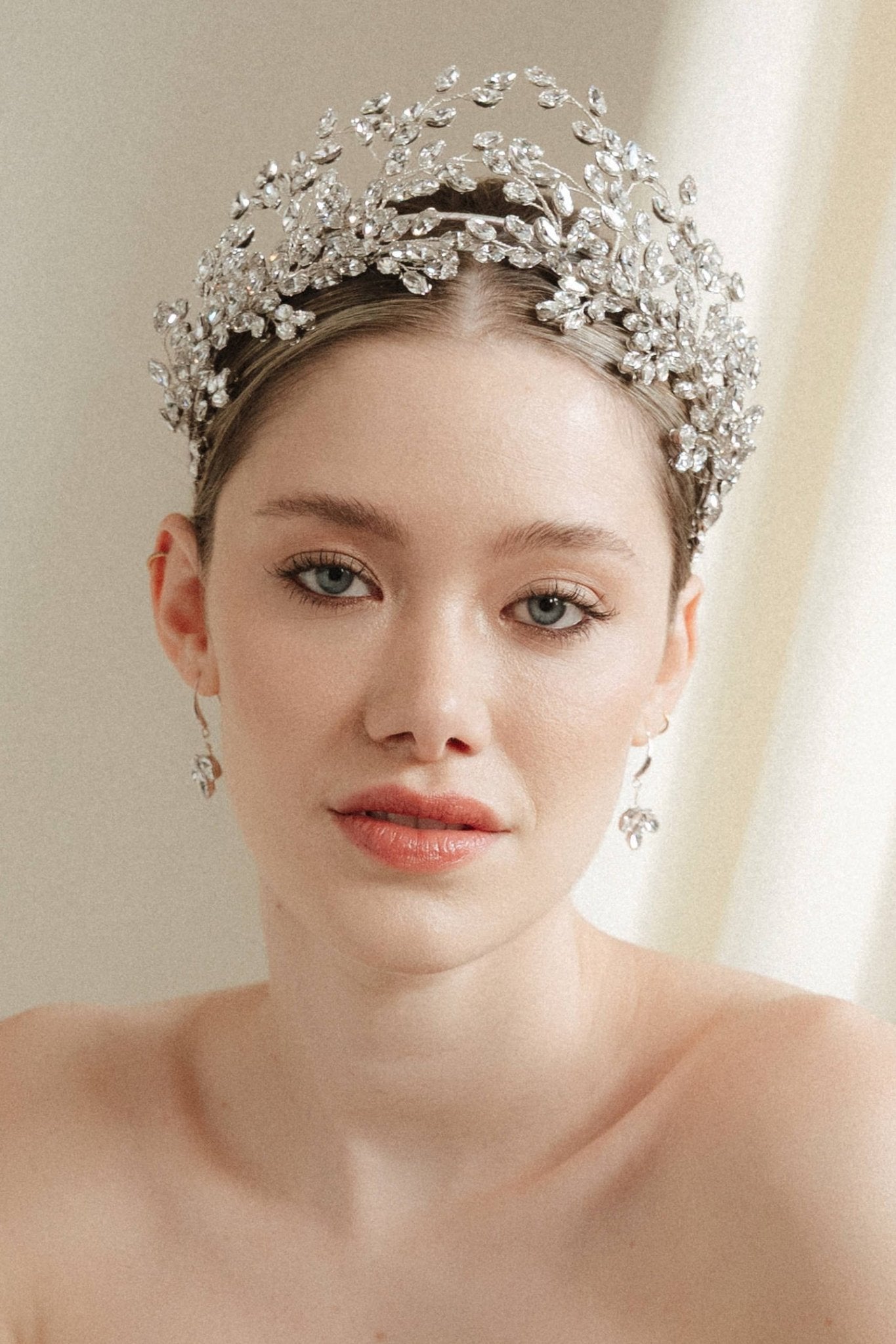a bride wears a set of two stacked silver crystal crowns with matching hair pins extending over the top of her head s if growing from the tiara style base.