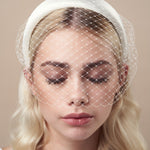 Ivory padded headband with adjustable birdcage veil worn above the mouth