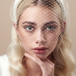 Ivory padded headband with adjustable birdcage veil worn above the mouth